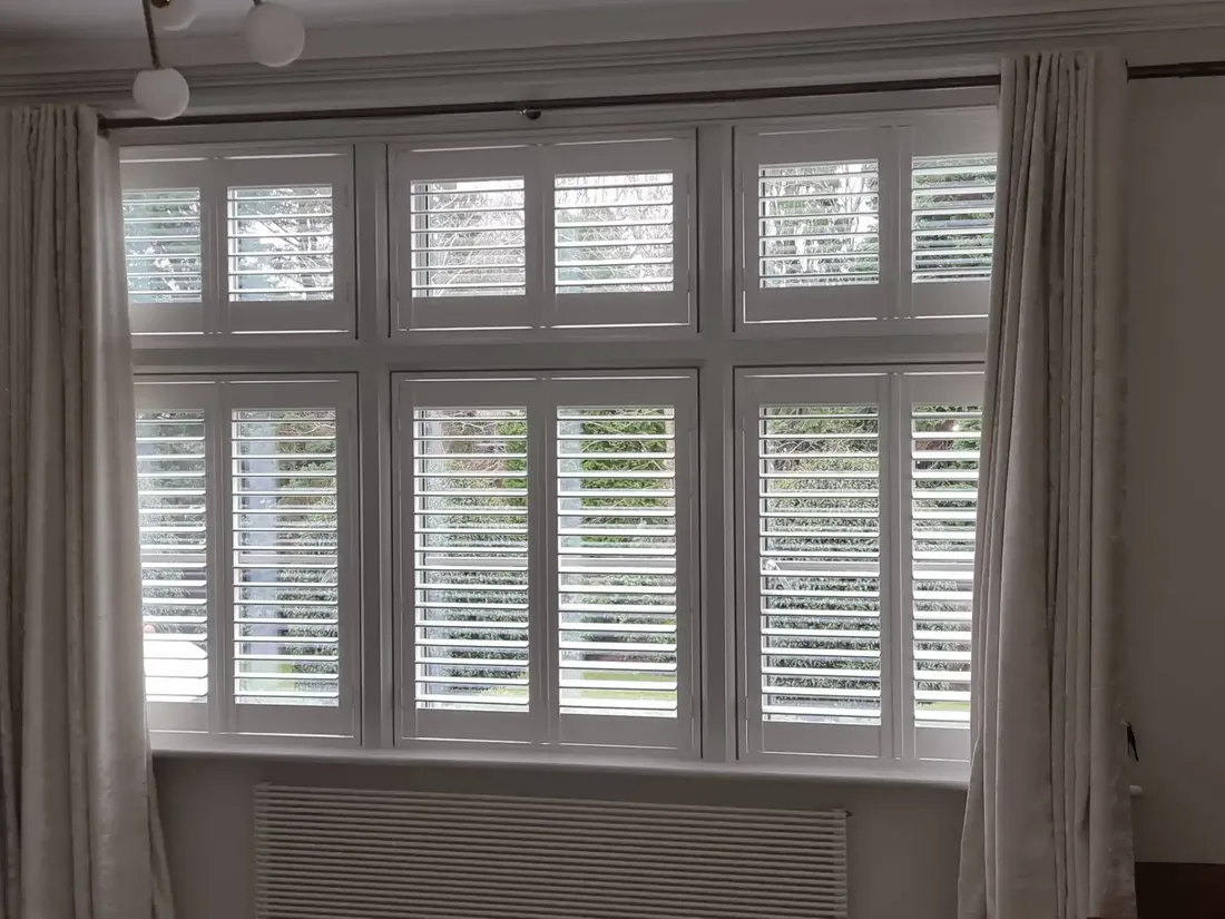 White full-height plantation shutters fitted across a bay window